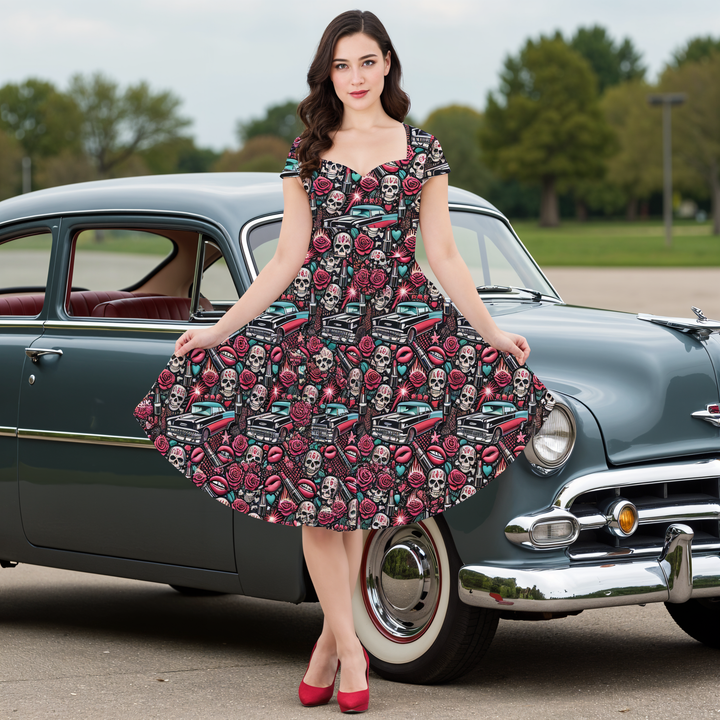 Model wearing a Rebel Rose cap sleeve midi dress with skull and rose print by a classic car, showcasing rockabilly style.