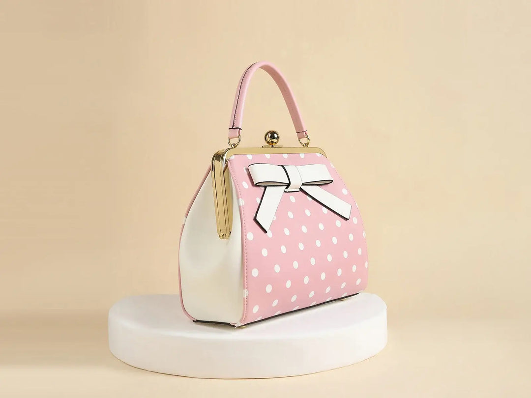 Pink polka dot rockabilly handbag with white bow, featuring a vintage kiss-lock closure.