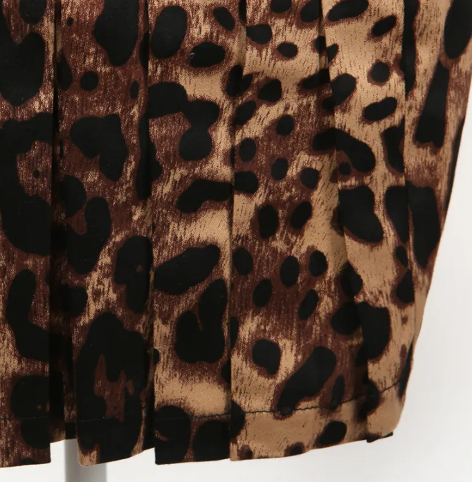 Close-up of leopard print fabric featuring pleats on a stylish pencil skirt, highlighting its bold design and texture.